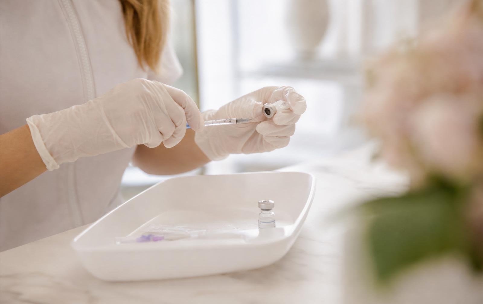 Cosmetic nurse in gloves preparing a small medical vial and fine syringe on a clean tray